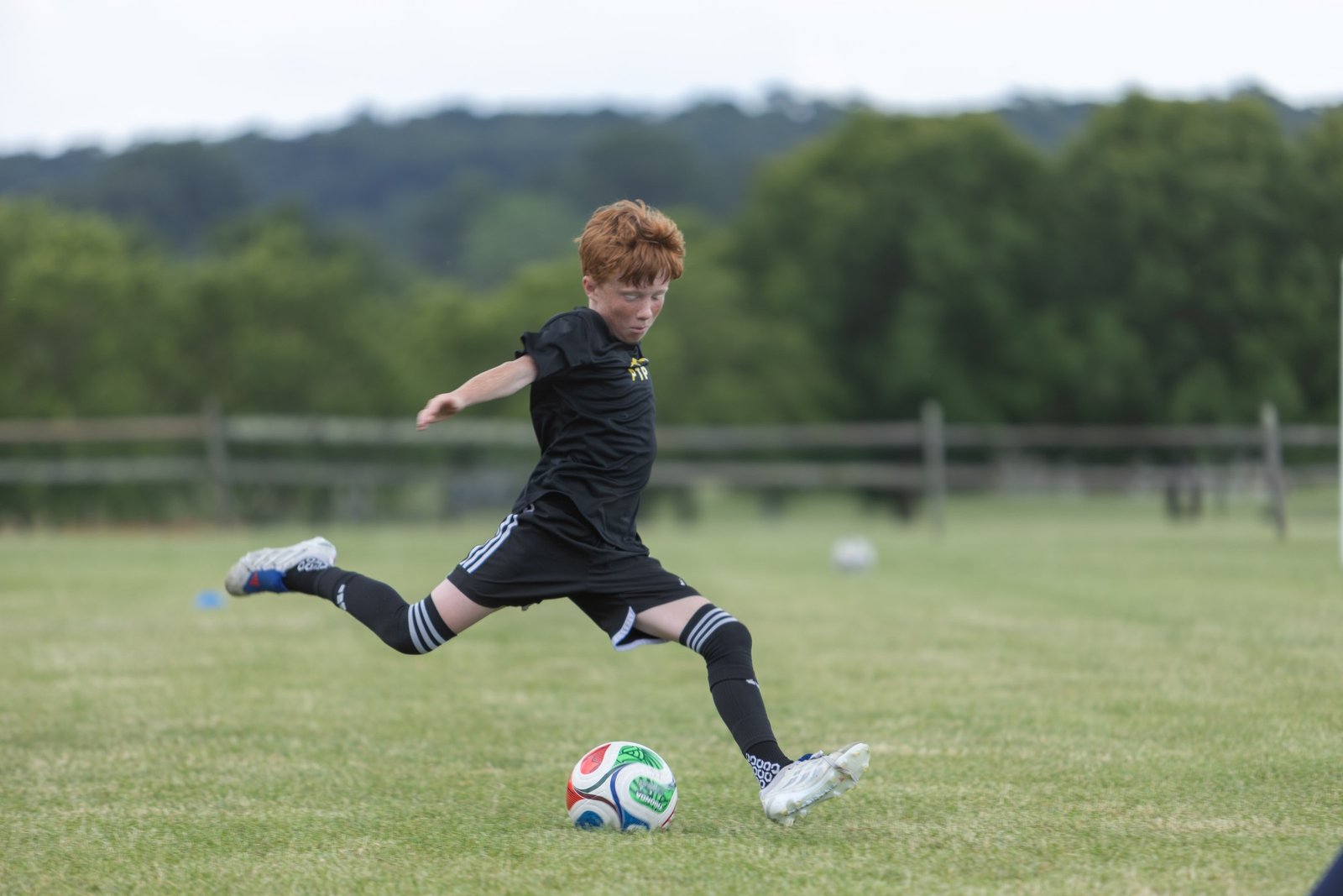 Camper in a black kit kicks the ball during a field