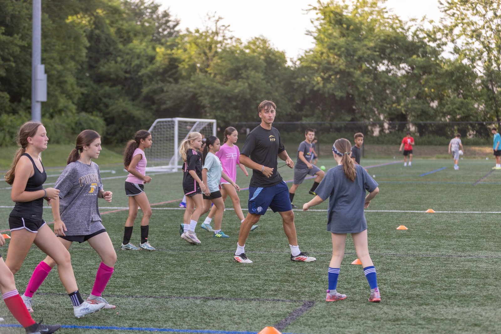 Campers and coaches move among small goals on an artificial turf